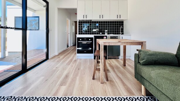Eine moderne Küche mit weißen Schränken, einem Holztisch und einem grünen Sofa.