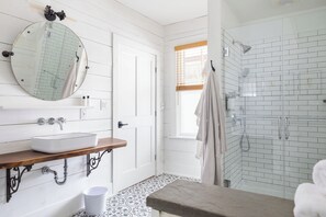 A bathroom with a white sink, wooden vanity, a large mirror, a shower with glass doors, and patterned floor tiles. - Howland House (Mount Tremper)