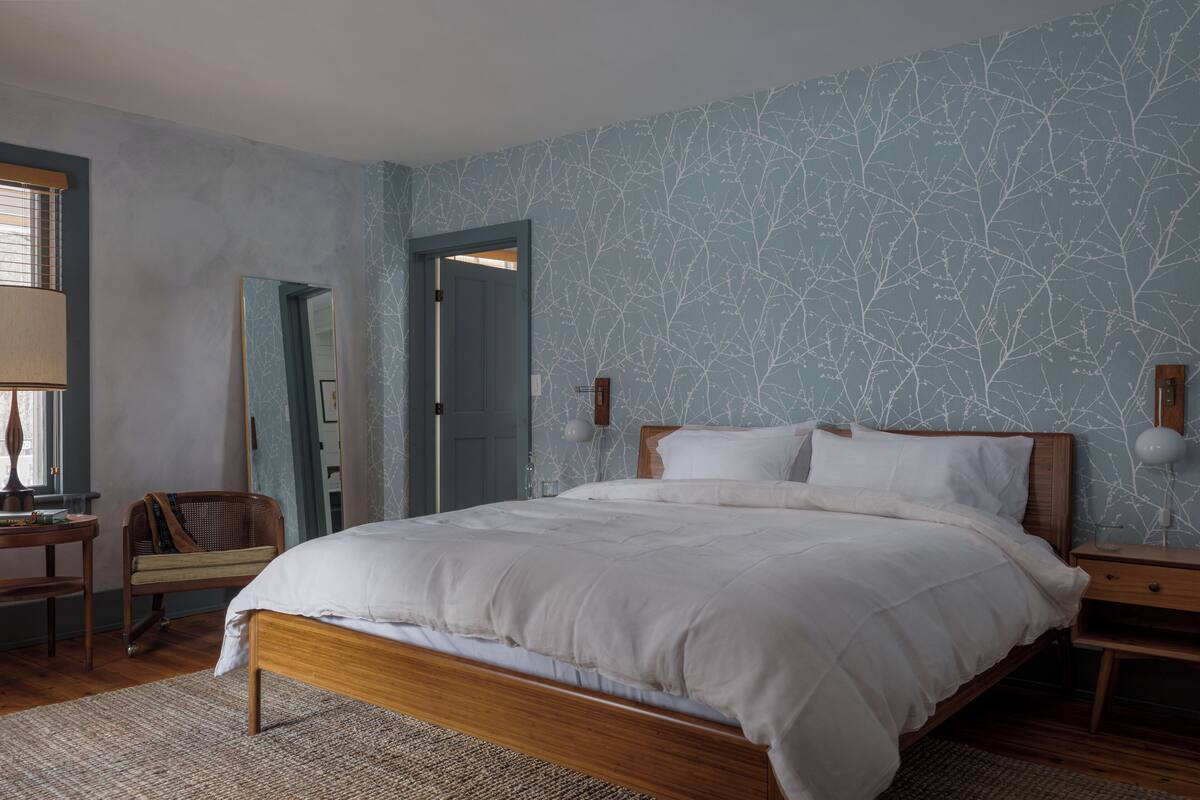 Una camera da letto con un letto in legno, un comodino, una sedia, uno specchio e una porta.