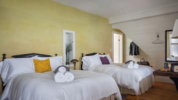 A hotel room with two beds, each with white bedding and a yellow pillow. There is a wooden floor and a mirror on the wall.