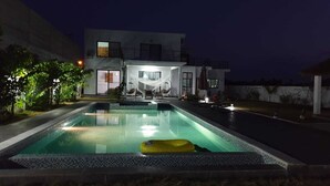 A modern house with a swimming pool, outdoor seating, and a well-lit patio area. - ASSINIE Oasis (Assinie)