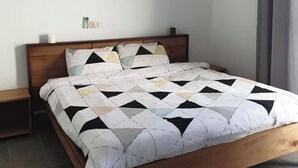 A bedroom with a wooden bed, a bedside table, a wall-mounted light, and a curtain. - ASSINIE Oasis (Assinie)