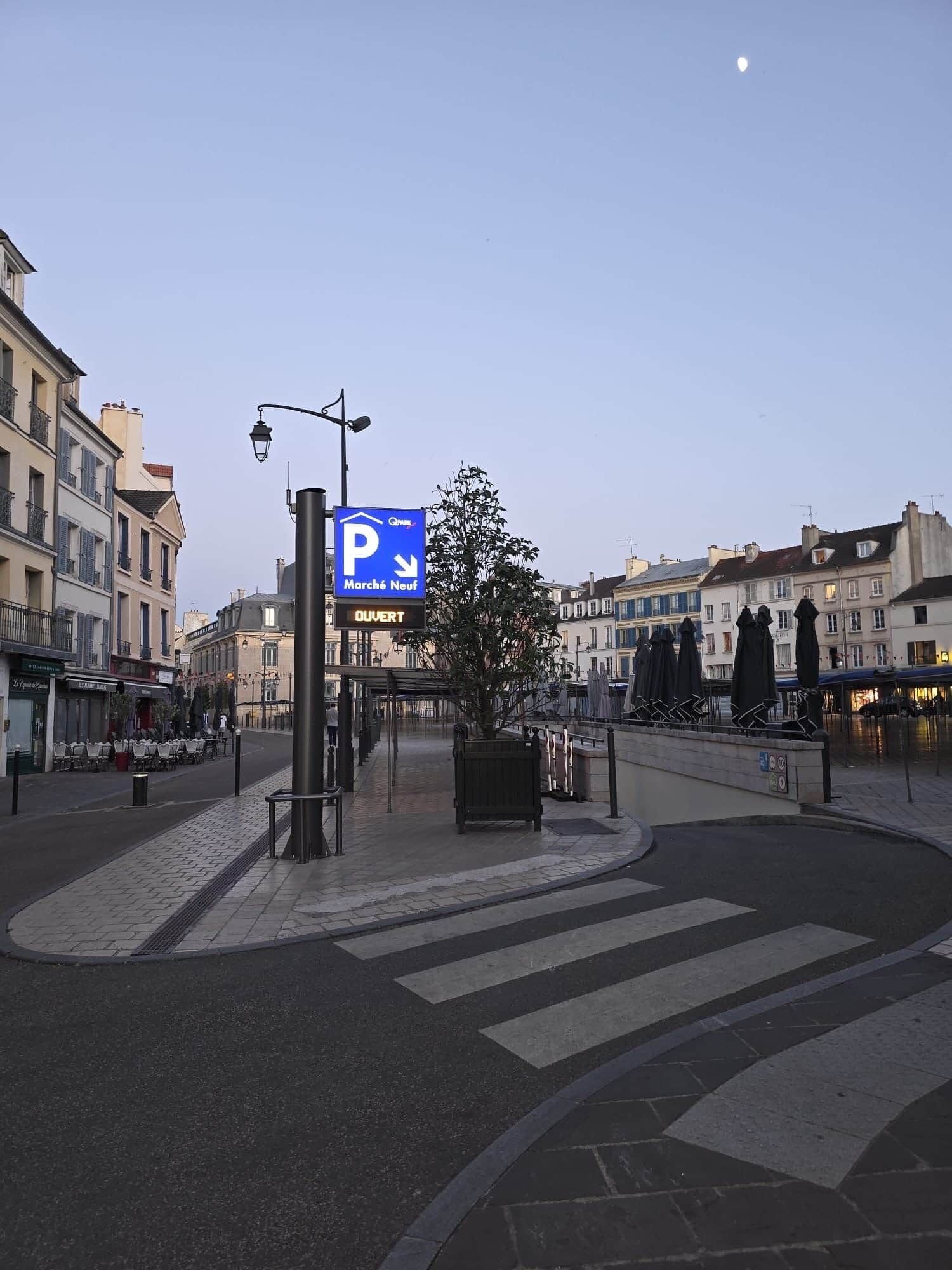 Een stadsweg met een blauw parkeersbord, een zebrapad en gebouwen op de achtergrond.