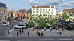 A street view with a building with multiple windows, a parking area, and a few people walking. - Studio Saint-Germain-en-Laye -RER A- Near Paris (Saint-Germain-en-Laye)