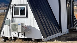 Een klein, gelijkvloers houten huisje met een zwart-wit gevel, een raam en een airconditioning aan de zijkant.
