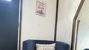Een kamer met een blauwe fauteuil en voetenbankje, een kleed, een bordje aan de muur, en een raam.