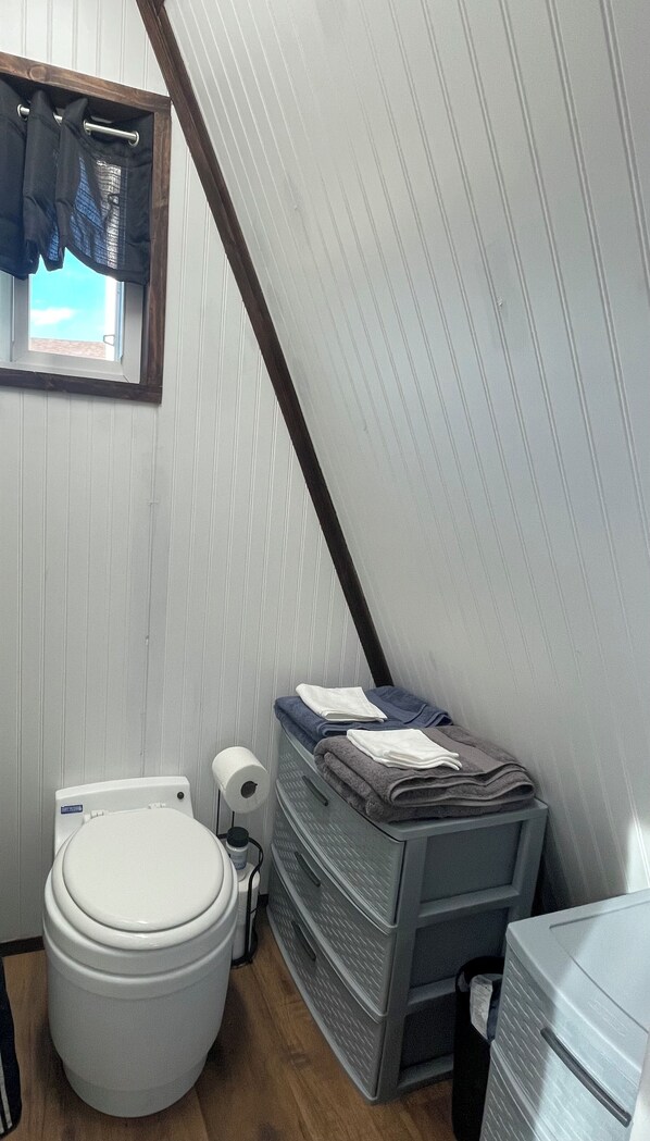A compact bathroom with a toilet, a small window with curtains, and a stack of towels on a metal rack.
