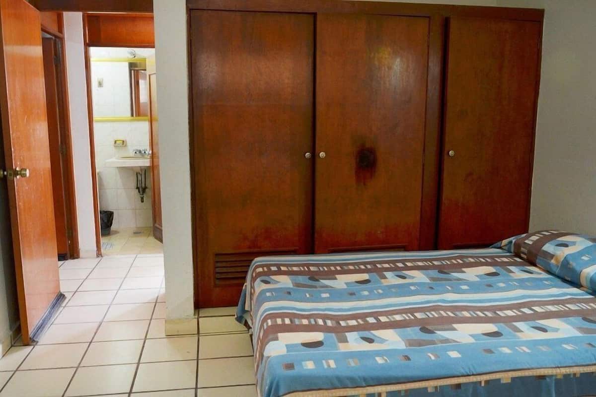 Ein Schlafzimmer mit Bett, Kleiderschrank und einem durchgegangenen Tür sichtbaren Badezimmer.