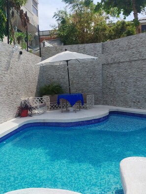 A swimming pool with a tiled edge, a lounge area with a table and chairs, and a covered seating area. - Suites Menavi (Acapulco)