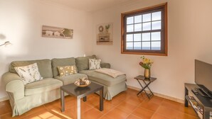 Un salon comprenant un canapé, une table basse, une petite table d’appoint avec un vase et un téléviseur.