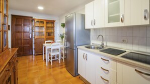 Une cuisine de taille réduite avec des meubles blancs, un réfrigérateur en acier inoxydable et un coin repas comprenant une table et des chaises.