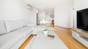 Een moderne woonkamer met een grijze bank, een salontafel met een schaakspel en een tv op een houten dressoir.