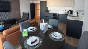 Una sala de estar moderna con una mesa de comedor lista para cuatro personas, un sofá y un televisor de pantalla plana montado en la pared.