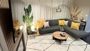 Un salon moderne avec un canapé d’angle, une table basse et une grande plante.