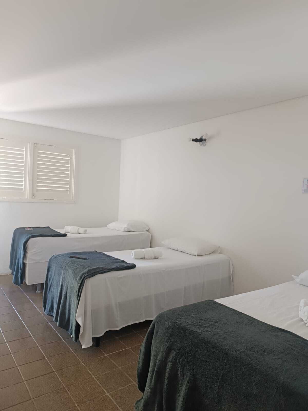 A room with three beds, white walls, a window with blinds, and a ceiling light.