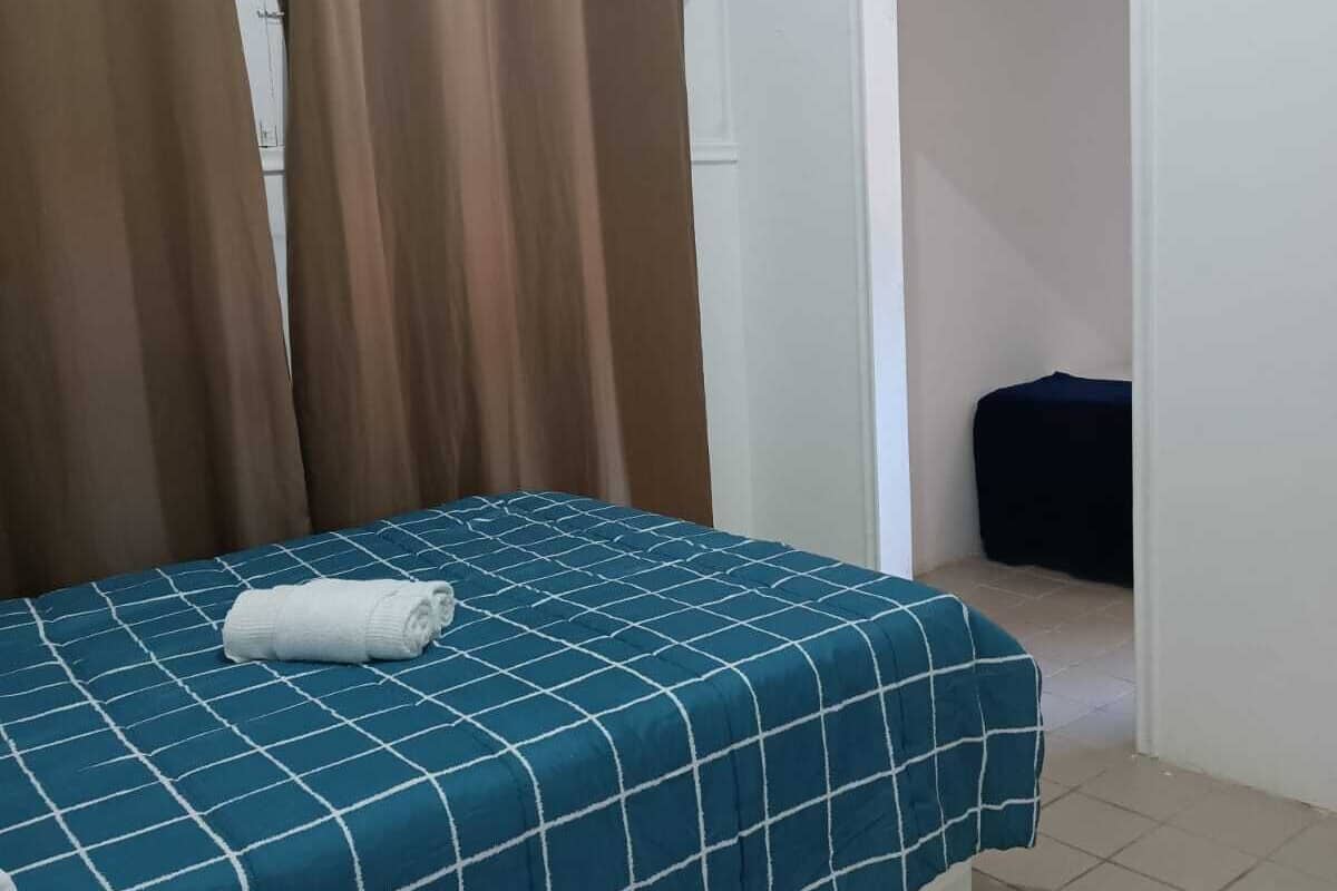 Une chambre à coucher comprenant un lit, des rideaux, un appareil de climatisation et une porte donnant sur une autre pièce.