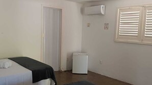 A room with two beds, a white door, an air conditioning unit, a window with blinds, and a white trash bin. - Pousada Oasis Tamandare (Tamandaré)