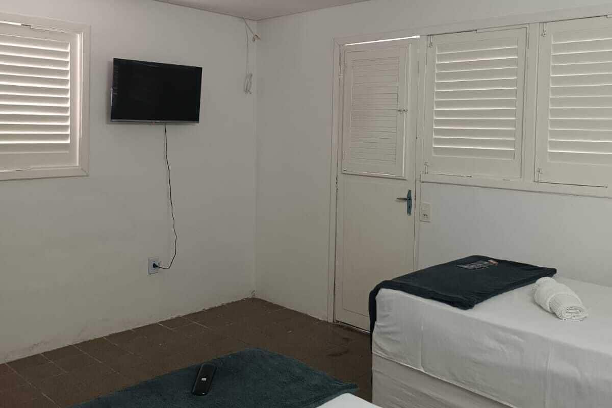 Une chambre avec deux lits, un téléviseur fixé au mur et une porte avec des volets.
