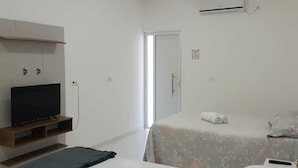 A hotel room with two beds, a TV on a wooden stand, an air conditioning unit, and a door leading to a balcony. - Pousada Oasis Tamandare (Tamandaré)