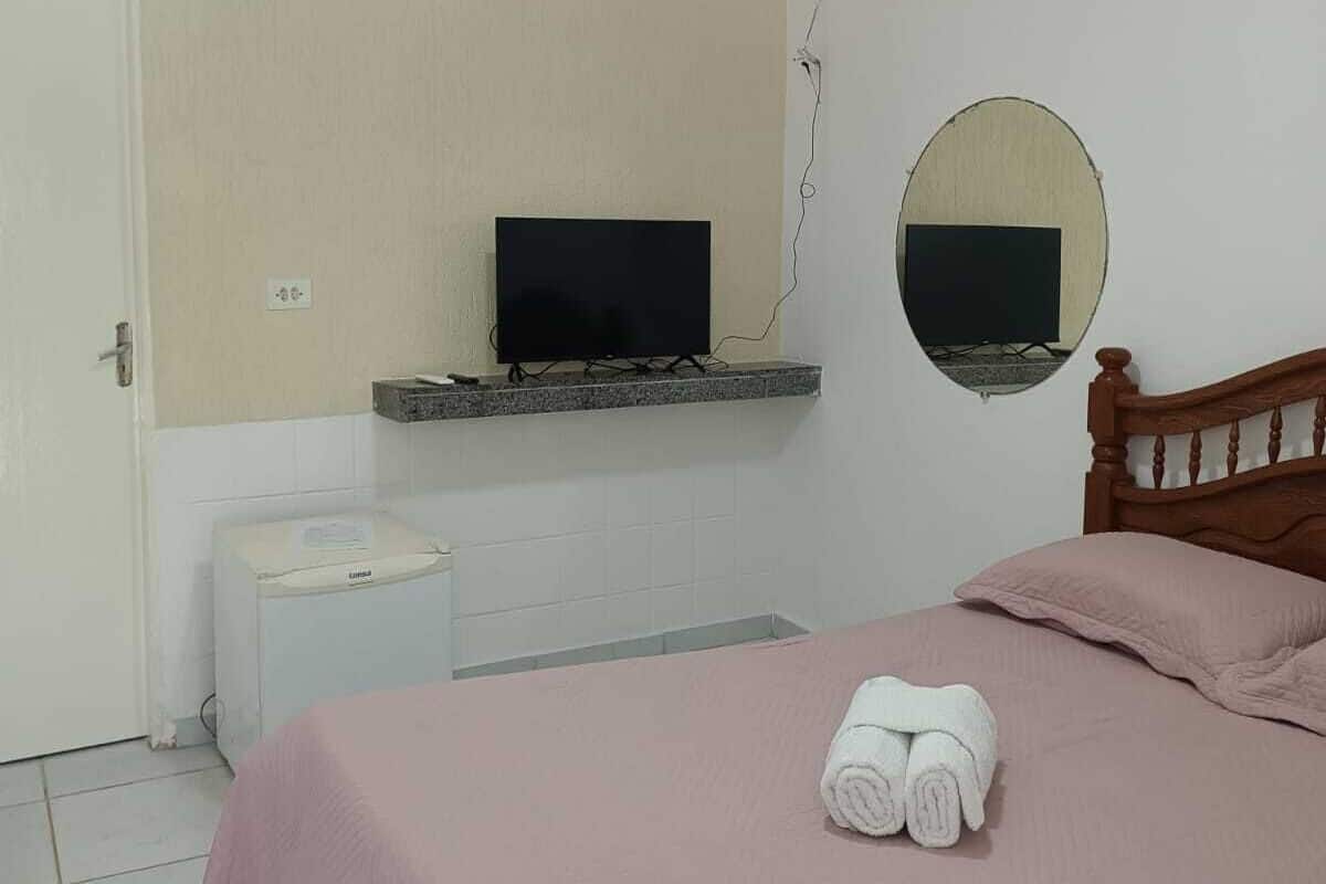 Une chambre à coucher avec un lit, une télévision, un miroir, une petite table et une porte.