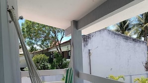 A balcony with a hammock, a tiled floor, and a view of buildings and trees. - Pousada Oasis Tamandare (Tamandaré)