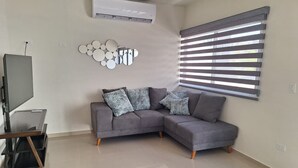 A modern living room with a grey sectional sofa, a flat-screen TV, and a wall-mounted mirror. - Casa Nopal (La Paz)