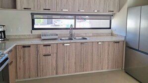 A modern kitchen with wooden cabinets, a stainless steel refrigerator, and a window providing natural light. - Casa Nopal (La Paz)