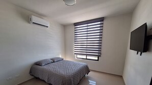 A bedroom with a bed, an air conditioner, a window with blinds, and a TV mounted on the wall. - Casa Nopal (La Paz)
