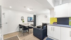 A modern kitchen with white cabinets, a dining area with a table and chairs, and a living area with a sofa. - London 3 Bedroom Cosy Clean Home Sleeps 6 Stratford Excel Modern (London)