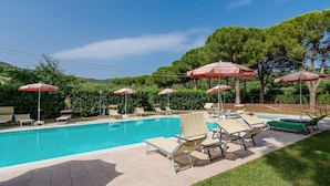 Ein Pool mit Liegestühlen und Sonnenschirmen, umgeben von Grünflächen und Bäumen.