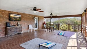 A covered patio with a brick wall, ceiling fans, a wooden table and chairs, a small table with a mat, and a view of trees through large windows. - 3 Bedroom Mid Century Brick Ranch Upstairs Home Near Smokies (Sevierville)