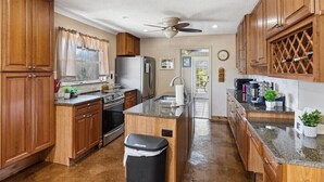A kitchen with wooden cabinets, a granite countertop, a refrigerator, an oven, and a ceiling fan. - 3 Bedroom Mid Century Brick Ranch Upstairs Home Near Smokies (Sevierville)