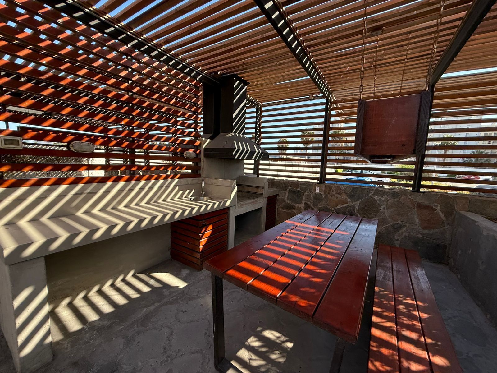 An outdoor patio with a stone wall, a wooden table, and a grill area.