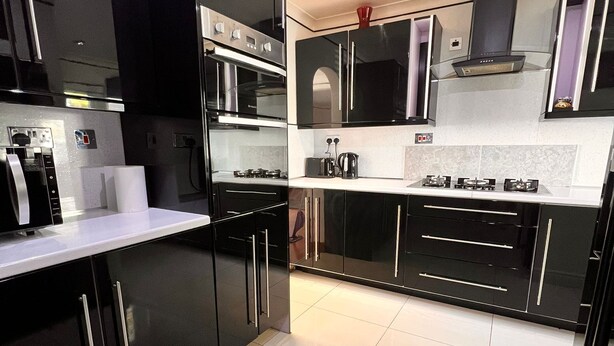 Une cuisine moderne avec des meubles noirs, des appareils en acier inoxydable et un plan de travail blanc.