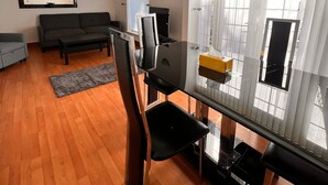 Un salon moderne avec une table à manger en verre, des chaises noires, un canapé gris et un téléviseur à écran plat fixé au mur.