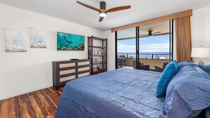 Un dormitorio con una cama grande, un ventilador de techo, una estantería y vista al océano.