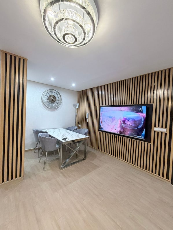 A modern dining area with a wooden panel wall, a round wall clock, and a flat-screen TV mounted on the wall.