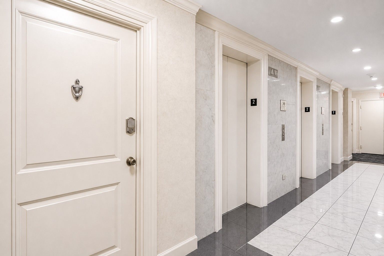 Un couloir d’hôtel avec des portes blanches, numérotées selon les étages, et un sol carrelé.