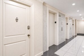 Corredor de hotel com portas brancas, numeradas por andar, e chão de azulejos.