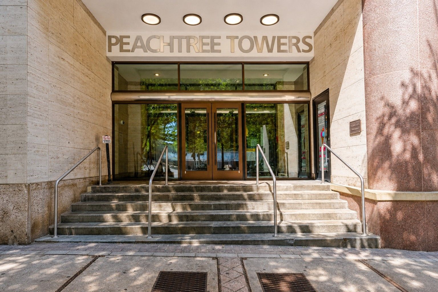 The entrance to Peachtree Towers with a glass door, metal handrails, and a set of stone steps leading up to the entrance.