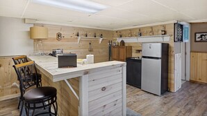 Cocina compacta con barra de madera, un refrigerador y estantes con botellas.