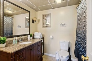 Baño con un espejo grande, lavamanos con encimera de granito, inodoro y cortina de ducha con estampado geométrico.