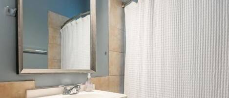 Un baño con tocador blanco, espejo, inodoro y cortina de ducha.