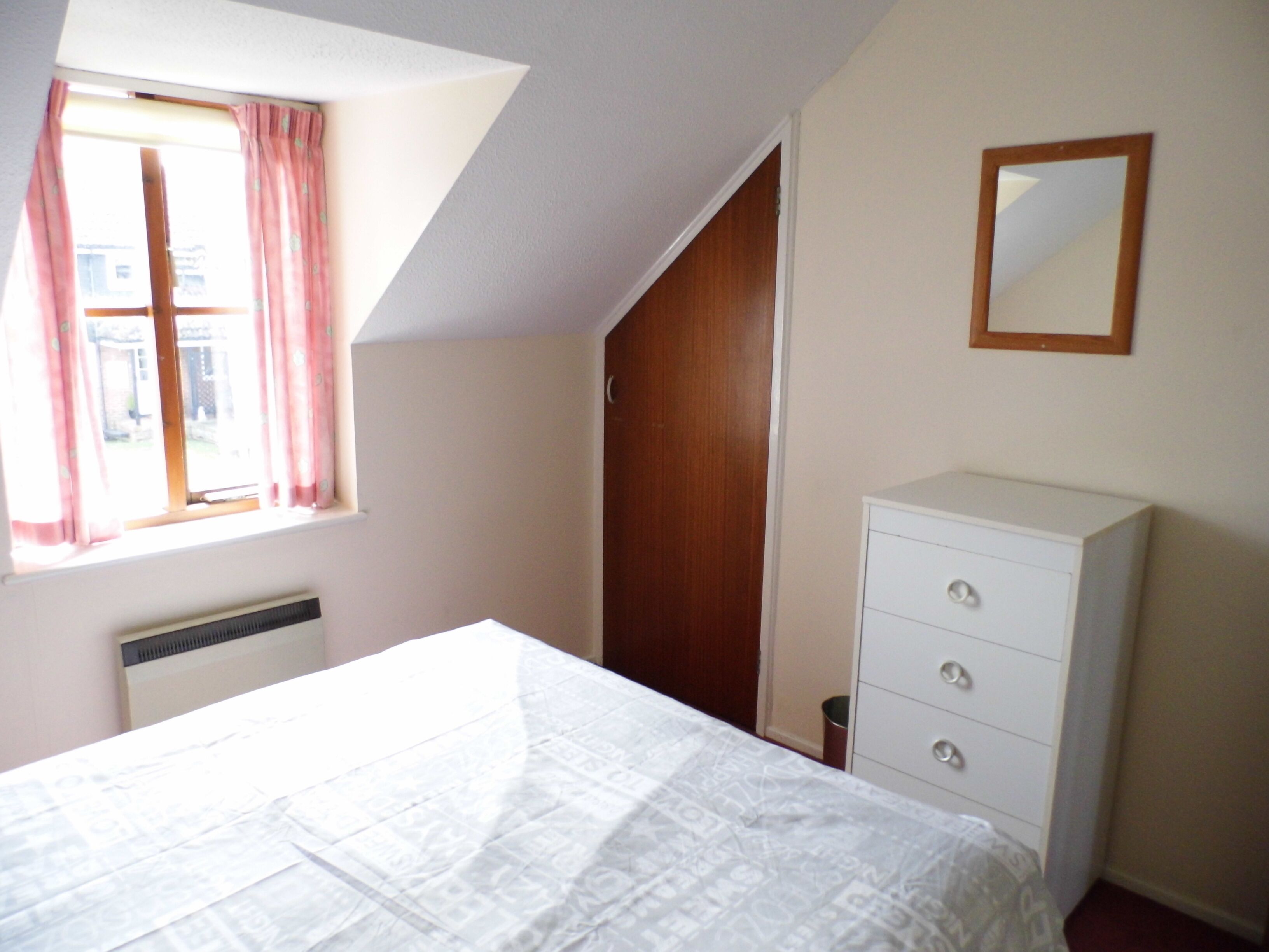 A bedroom with a bed, a dresser, a window with curtains, and a door.