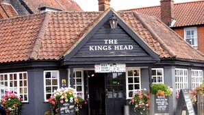 Un pub chiamato "The King's Head" con una facciata tradizionale in legno nero, tetto a tegole e composizioni floreali all'ingresso.