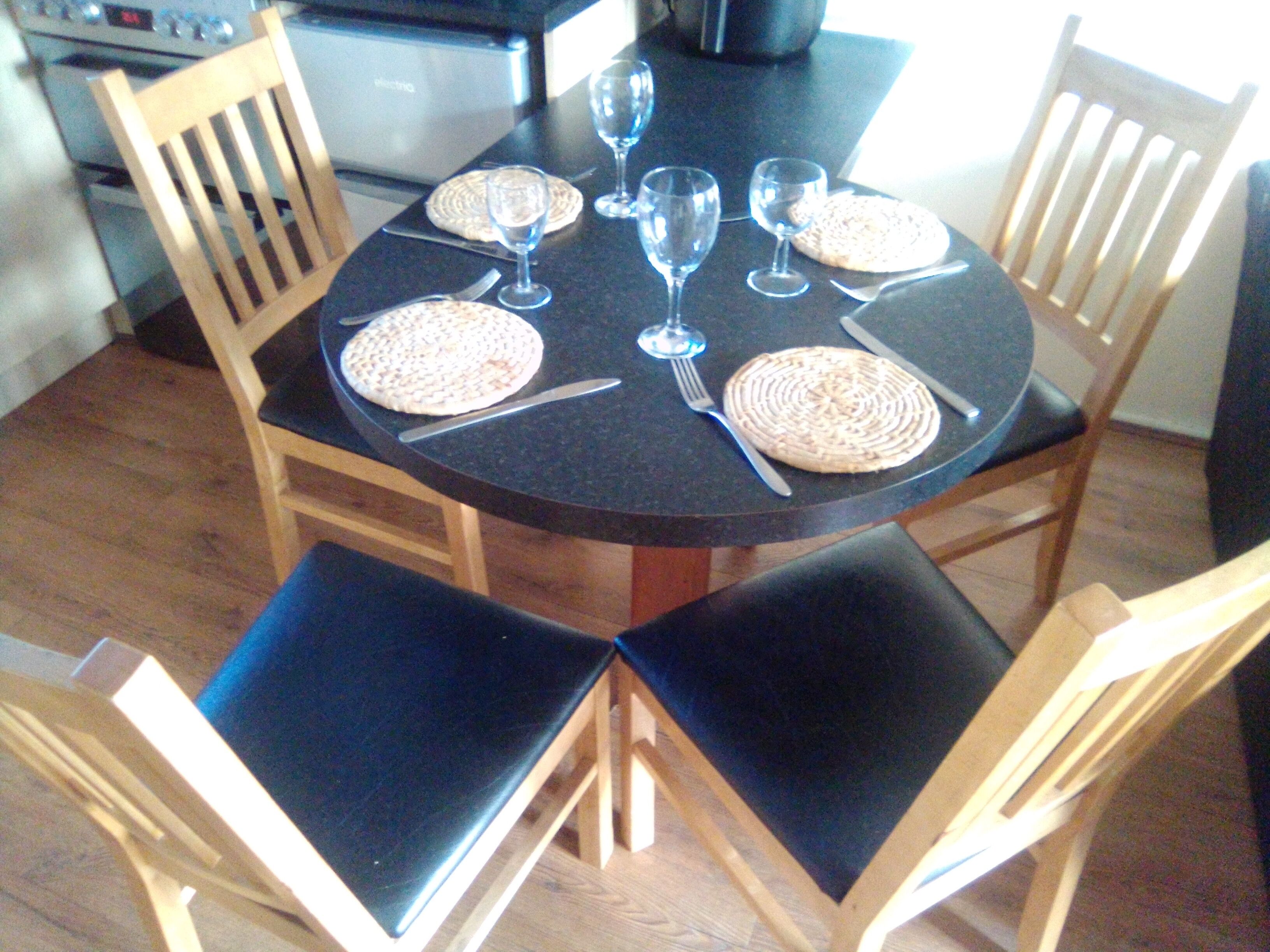 A round dining table with four chairs, each with a woven placemat and cutlery.