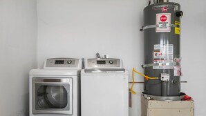 Zwei weiße Waschmaschinen und ein großer, grauer Warmwasserbereiter in einem Raum mit einer schlichten weißen Wand.