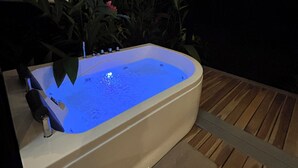 Tinaja exterior con cubierta de madera, rodeada de plantas y luces colgantes.