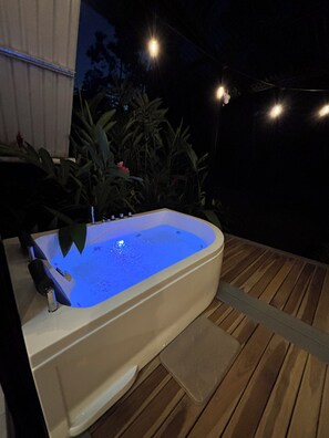 Een buitendouche met een houten terras, omringd door planten en lichtjes.