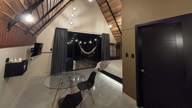 Un interior moderno con una mesa de comedor de cristal, sillas negras, una hamaca y una cama grande.